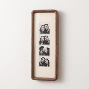 Peut inclure: Un cadre photo en bois avec un passe-partout crème contient quatre photos de style photomaton en noir et blanc d'un couple. Le cadre a des bords arrondis et est monté sur un mur blanc.