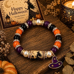 Könnte beinhalten: Ein Perlenarmband mit abwechselnden violetten, schwarzen und orangefarbenen Perlen, akzentuiert durch klare Strasssteine und weiße Perlen. Eine zentrale zylindrische Perle zeigt eine Hexensilhouette und ein violetter Hexenhutanhänger.