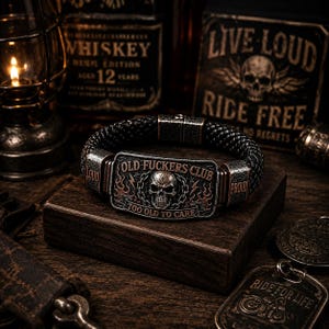 May include: A black braided bracelet featuring a rectangular metal plate with a skull graphic, flame details, and the text "OLD FUCKERS CLUB" and "TOO OLD TO CARE". The metal side accents are engraved with the words "LOUD" and "PROUD" in a dark finish.