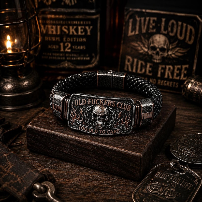 May include: A black braided bracelet featuring a rectangular metal plate with a skull graphic, flame details, and the text "OLD FUCKERS CLUB" and "TOO OLD TO CARE". The metal side accents are engraved with the words "LOUD" and "PROUD" in a dark finish.