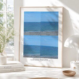 May include: A framed wall art print featuring a four-panel grid of Enoshima Beach, Japan. The image displays a blue ocean, sandy shoreline, and a pier. Below the grid, the text reads: ENOSHIMA BEACH, JAPAN. SOMEONE, SOMEWHERE, IS WAITING FOR YOUR LIGHT.