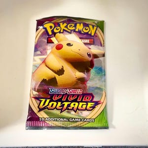 May include: A sealed Pokémon trading card booster pack from the Sword & Shield Vivid Voltage series. The packaging features a yellow Pikachu character, the Pokémon logo, and the text 10 ADDITIONAL GAME CARDS printed on the front of the wrapper.