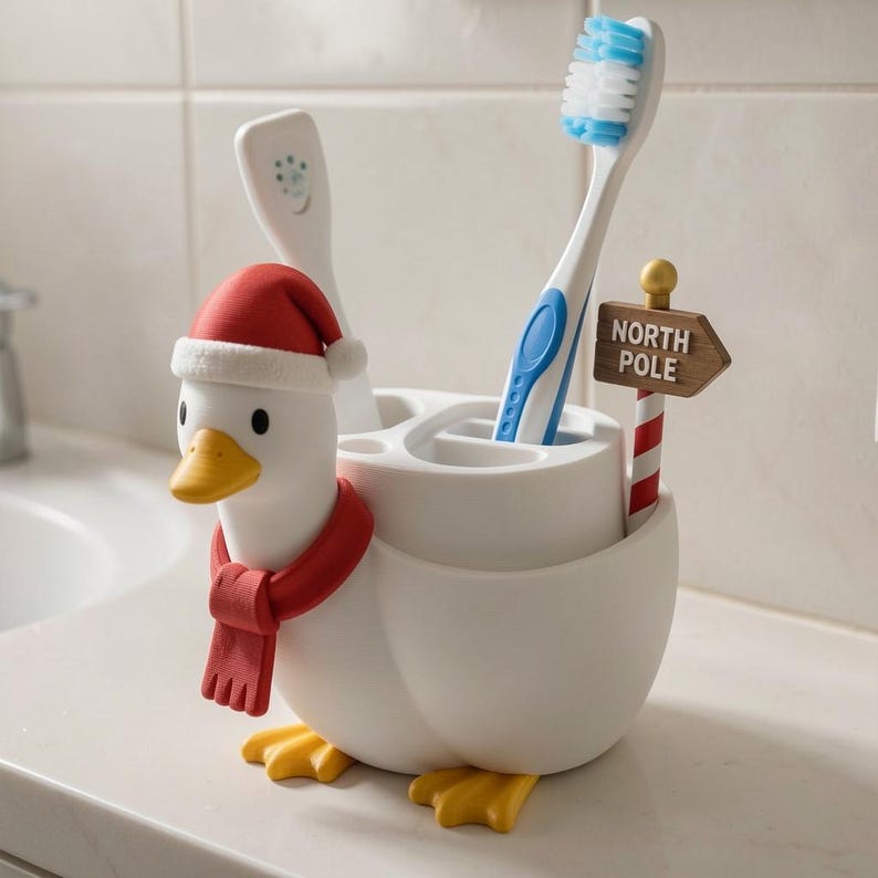 May include: A white duck-shaped toothbrush holder featuring a red Santa hat, a red scarf, and yellow feet. The holder has multiple compartments for toothbrushes and includes a small brown signpost with the text NORTH POLE in white letters.