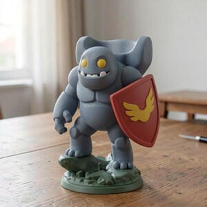 May include: A gray figurine of a cartoon character with a shield. The figure has a smiling face with yellow eyes and a cape. The red shield features a gold emblem. The figurine is on a green base, and the overall design is whimsical.