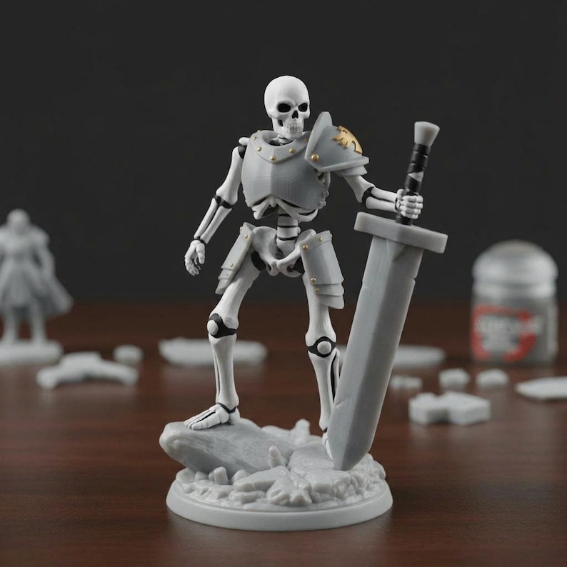 Puede incluir: Una figura de guerrero esqueleto gris y blanco, sosteniendo una espada grande. La figura lleva una armadura con detalles dorados y se encuentra sobre una base rocosa. Otras figuras en miniatura y pintura est&aacute;n en el fondo. Este es un objeto de colecci&oacute;n de tem&aacute;tica fant&aacute;stica.