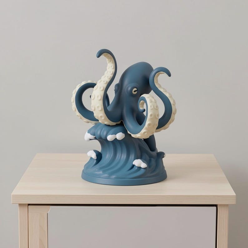 Op de afbeelding: Een blauw octopusbeeldje met cr&egrave;mekleurige tentakels, bovenop een gestileerde blauwe golf. De decoratieve octopus is waarschijnlijk gemaakt van keramiek of hars en staat op een lichtgekleurd houten oppervlak.