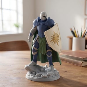May include: A detailed figurine of a knight in blue armor, a white helmet, and a green cape, holding a shield with a sun design. The figurine stands on a gray stone base, placed on a wooden table. The background includes a window and a pencil holder.