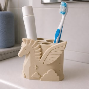 Op de afbeelding: Een beige tandenborstelhouder in de vorm van een gevleugeld paard, voorzien van reli&euml;fdetails van wolken en sterren. De houder bevat een witte tandpastatube en een blauw-witte tandenborstel met blauwe haren, rechtop in de ronde openingen.
