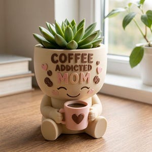 May include: A beige planter shaped like a seated figure holding a small pink mug with a brown heart. The planter features the text COFFEE ADDICTED MOM in brown and pink letters, accented with small pink hearts and brown coffee bean shapes.