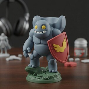 May include: A gray figurine of a smiling, muscular creature with yellow eyes and a shield featuring a yellow wing design. The figurine stands on a green base with a rock-like texture. The shield is red.