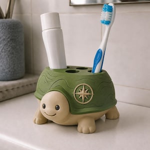 May include: A turtle-shaped bathroom organizer in olive green and beige. The shell features a compass rose emblem and four circular openings for storage. A white toothpaste tube and a blue and white toothbrush are inserted into the holder.