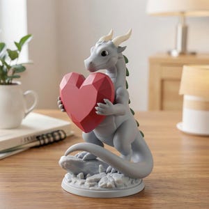 Peut inclure: Figurine de dragon gris tenant un c&oelig;ur rouge facett&eacute;. Le dragon a de petites cornes et des accents verts sur le dos. La figurine est sur une base ronde et textur&eacute;e. Objet d&eacute;coratif.