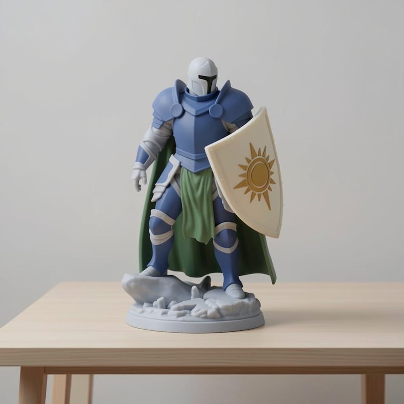 May include: A figurine of a knight in blue armor, a white helmet, and a green cape. The knight holds a shield with a gold sun design. The figurine is standing on a gray stone base, and is on a light brown wooden table.