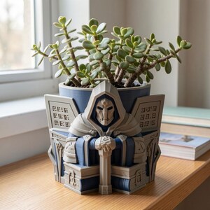 K&ouml;nnte beinhalten: Ein blau-hellgrauer 3D-gedruckter &Uuml;bertopf mit einer geharnischten Kapuzenfigur, die ein Schwert h&auml;lt. Der &Uuml;bertopf hat geometrische Seitenteile mit eingravierten quadratischen Symbolen und enth&auml;lt eine gr&uuml;ne Sukkulente mit runden Bl&auml;ttern.