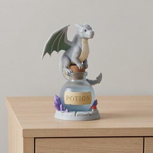 以下が含まれることがあります： ファンタジーをテーマにした置物。灰色のドラゴンがポーションボトルの上に座っています。ボトルにはコルク栓があり、「POTION」と書かれたラベルが付いています。ベースには紫色のクリスタルと赤いキノコが含まれています。ドラゴンは緑色の裏地付きの翼を持っています。