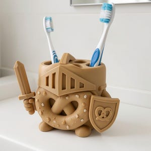 May include: A tan, pretzel-shaped toothbrush holder designed like a knight, featuring a helmet visor, a sword held in one hand, and a shield with a pretzel emblem. The holder has multiple circular openings for toothbrushes and stands on small feet.