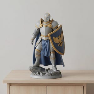 May include: A gray knight figurine with gold accents, wearing armor and a blue cape. The knight holds a shield with a gold eagle emblem. The figurine stands on a rocky base, a decorative item.