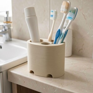 May include: A beige toothbrush holder with a tube of toothpaste and three toothbrushes. The toothbrushes have white handles with blue and green bristles. The holder is cylindrical with a ridged texture and four circular openings.