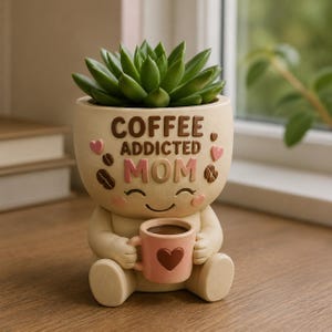 May include: A beige ceramic planter shaped like a seated figure holding a small pink mug with a heart. The planter features the text COFFEE ADDICTED MOM in raised brown and pink letters, decorated with small pink hearts and brown coffee beans.