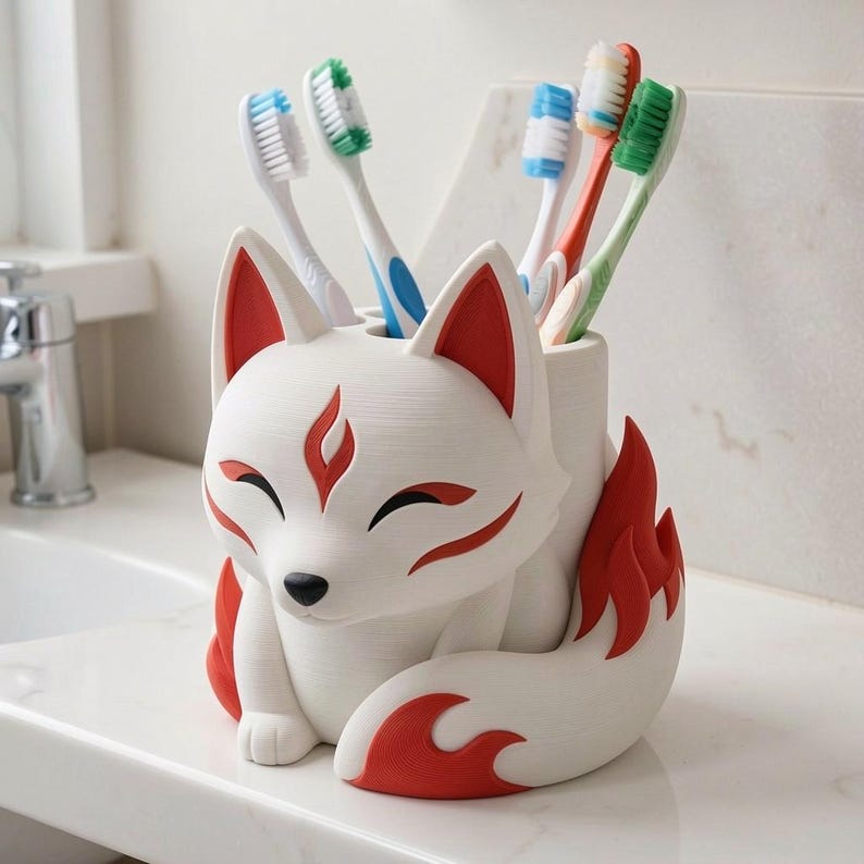 May include: A white and red fox-shaped toothbrush holder with a smooth finish. The fox has closed eyes, pointed ears, and a large curled tail. It contains four toothbrushes with blue, green, and orange bristles standing upright in the holder.