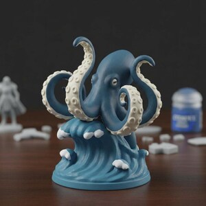 Op de afbeelding: Een blauw octopusbeeldje met witgepunte tentakels, bovenop een gestileerde blauwe golf. De octopus heeft een gedetailleerde textuur. Het beeldje is waarschijnlijk een decoratief item of onderdeel van een verzameling.