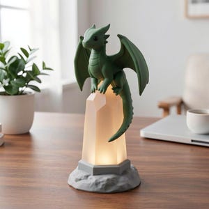 May include: A green dragon figurine perched atop a glowing, crystal-shaped lamp. The lamp has a gray base and a warm, soft light emanating from within. The dragon has detailed wings and a long tail, creating a fantasy-themed decorative piece.