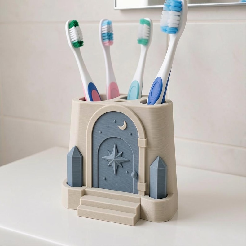 Pu&ograve; includere: Un portaspazzolini beige a forma di ingresso di castello con una porta blu decorata con un motivo a stella e luna crescente. Il supporto presenta quattro fori contenenti spazzolini con setole e manici verdi, rosa, turchesi e blu.