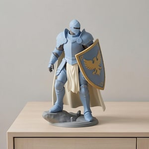 May include: A light blue knight figurine with a helmet, armor, and a shield. The shield features a gold eagle design. The knight stands on a gray base with a rock-like texture, and wears a white cape. The figurine is displayed on a light wood surface.