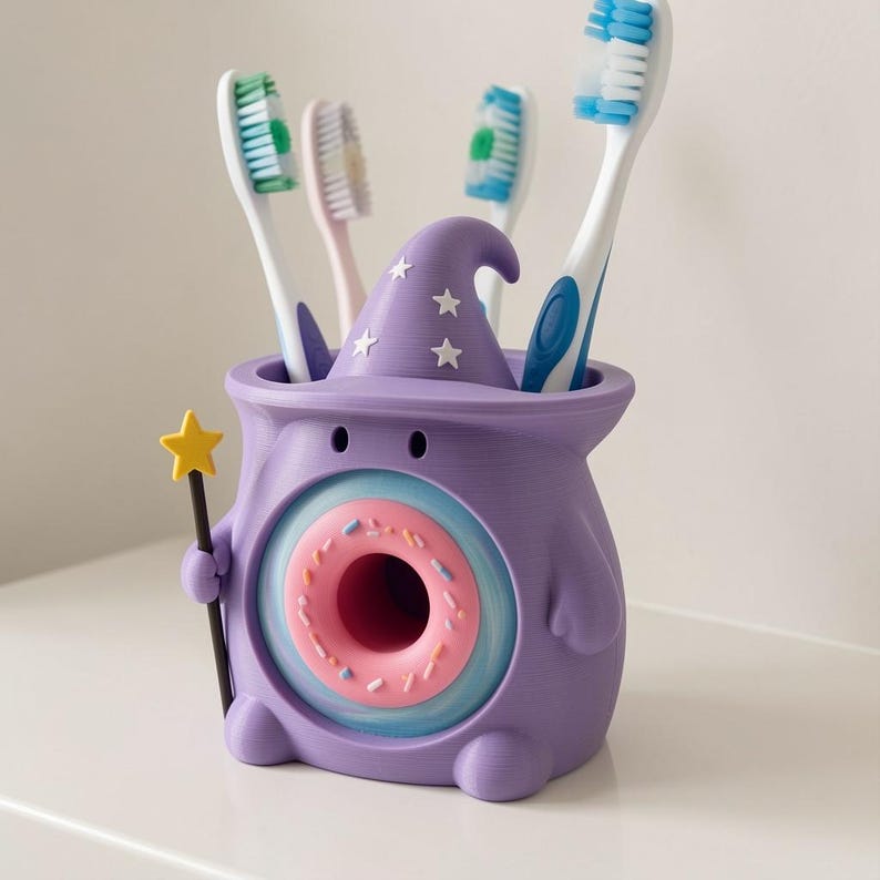 May include: A purple toothbrush holder shaped like a creature wearing a wizard hat with white star accents. The front features a pink donut graphic with sprinkles. The creature holds a yellow star wand. Four toothbrushes are inserted inside.