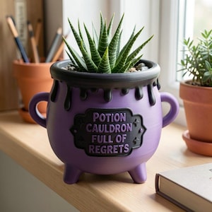 May include: A purple cauldron-shaped planter with two handles and three feet, featuring a black rim with a dripping design. A black plaque on the front displays the text POTION CAULDRON FULL OF REGRETS in purple lettering. A green succulent plant sits inside.