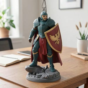 May include: A teal and red knight figurine with a smiling face, wearing armor and holding a shield with a gold eagle emblem. The figurine stands on a gray base and has a red cape. A chain is attached to the helmet.
