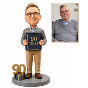 May include: A custom bobblehead figurine of an older person with glasses, a mustache, and light brown hair, wearing a grey V-neck sweater over a light blue shirt and tan trousers. The figure holds a blue book labeled 90 YEARS next to a gift box.
