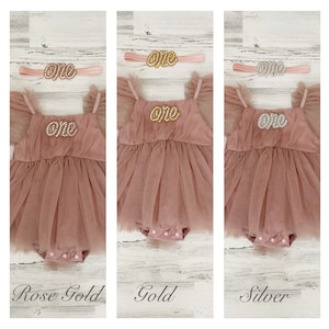 Peut inclure: Une barboteuse en tulle rose poudr&eacute; avec des manches &agrave; volants et un entrejambe &agrave; boutons-pression, accompagn&eacute;e d'un bandeau assorti. La barboteuse et le bandeau portent le mot "one" en &eacute;criture perl&eacute;e rose dor&eacute;, dor&eacute;e ou argent&eacute;e.