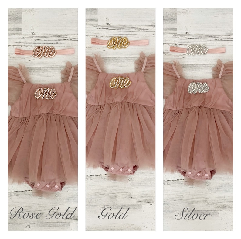 Peut inclure: Une barboteuse en tulle rose poudr&eacute; avec des manches &agrave; volants et un entrejambe &agrave; boutons-pression, accompagn&eacute;e d'un bandeau assorti. La barboteuse et le bandeau portent le mot "one" en &eacute;criture perl&eacute;e rose dor&eacute;, dor&eacute;e ou argent&eacute;e.