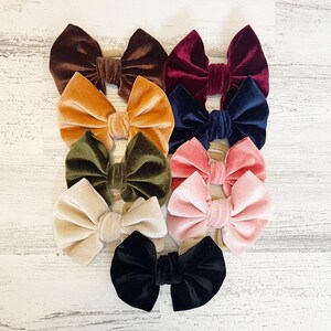 Könnte beinhalten: Sortiment aus Samt-Haarbändern in verschiedenen Farben, darunter Braun, Orange, Burgunderrot, Dunkelblau, Grün, Rosa, Beige und Schwarz. Die Schleifen sind in der Mitte mit einem Knoten gebunden und an einem hautfarbenen elastischen Haarreif befestigt.