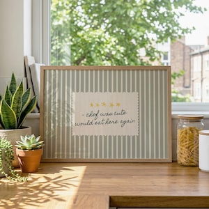 Peut inclure: Une impression encadrée rectangulaire avec un fond à rayures verticales vert sauge et blanc. Au centre, un écusson en tissu crème aux bords festonnés affiche cinq étoiles jaunes et le texte : - chef was cute would eat here again.