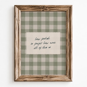 May include: A framed wall art piece featuring a sage green and white gingham pattern background. Centered is a rectangular cream-colored paper with scalloped edges, displaying the black cursive text: how foolish to forget how rare all of this is.