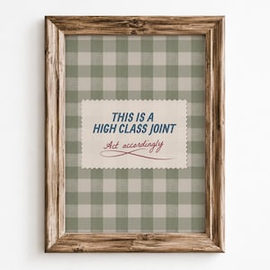 Peut inclure: Un cadre en bois rectangulaire contenant une impression à motif vichy vert sauge et blanc. Au centre, une carte festonnée crème porte le texte bleu THIS IS A HIGH CLASS JOINT et le texte cursif rouge Act accordingly.