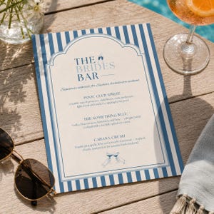 May include: A rectangular menu card with a blue and white vertical striped border. The text reads THE BRIDES BAR, followed by descriptions for Pool Club Spritz, The Something Blue, and Cabana Crush cocktails, featuring small illustrations of glasses.