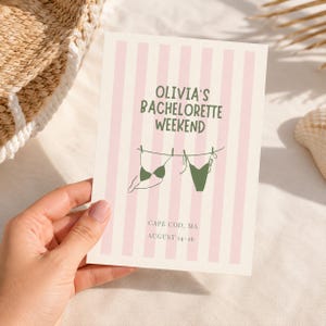 May include: A rectangular card with a light pink and white vertical striped background. The text reads OLIVIA'S BACHELORETTE WEEKEND in green, with a line drawing of two green bikinis hanging on a clothesline. Below, it says CAPE COD, MA AUGUST 14-16.