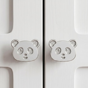 May include: Two silver-toned metal cabinet knobs shaped like panda faces. Each knob features a smooth, polished outline with textured, glittery silver inlays for the ears and eye patches, and a simple engraved nose and mouth detail.