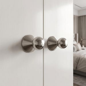 May include: Two brushed nickel cabinet knobs with a spherical head and a conical base mounted on white double doors. The hardware features a smooth metallic finish and a rounded profile, providing a functional grip for opening and closing doors.