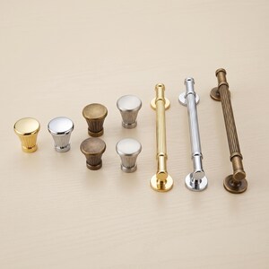 May include: A collection of cabinet hardware including four round knobs and three long bar pulls. The knobs and pulls feature fluted designs and come in polished gold, shiny chrome, brushed silver, and antique bronze metallic finishes.
