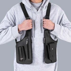Premium black leather shoulder holster bag and techwear chest rig with an adjustable X-strap design. Includes a vertical zipper pocket and a utility pouch with a silver snap button, shown isolated on a solid gray background.