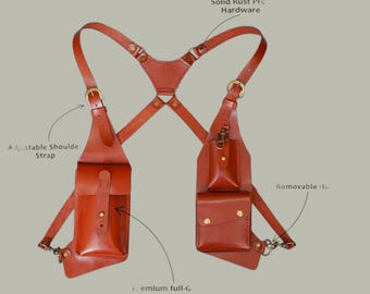 May include: A brown leather shoulder harness featuring two vertical pouches with flap closures, adjustable shoulder straps, solid rust-proof hardware, and removable hooks. The design includes multiple pockets secured with metal studs and buckles.