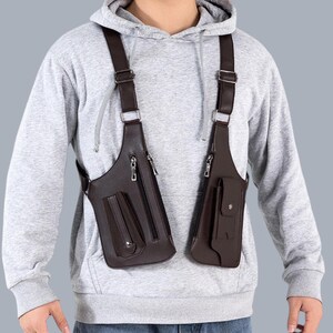 Premium black leather shoulder holster bag and techwear chest rig with an adjustable X-strap design. Includes a vertical zipper pocket and a utility pouch with a silver snap button, shown isolated on a solid gray background.