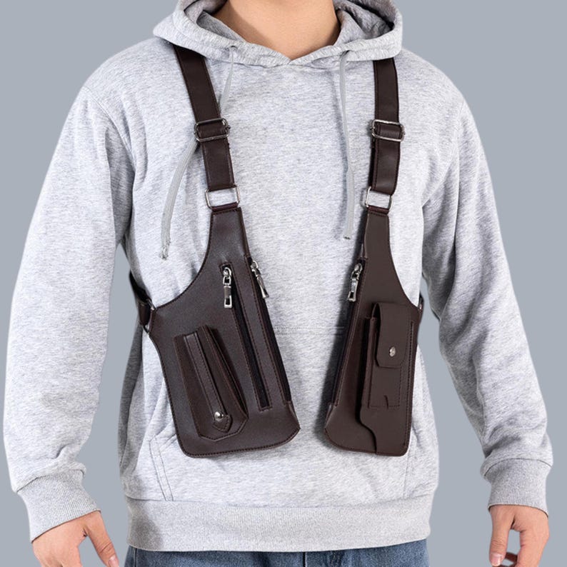 Premium black leather shoulder holster bag and techwear chest rig with an adjustable X-strap design. Includes a vertical zipper pocket and a utility pouch with a silver snap button, shown isolated on a solid gray background.