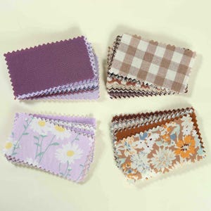 May include: Four stacks of rectangular fabric swatches with pinked edges. One stack is solid purple, one features a brown and white gingham check, one displays a light purple floral pattern with white daisies, and one shows a brown floral print.