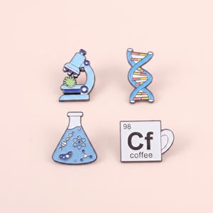 May include: A set of four enamel pins featuring science themes: a blue microscope with a green microbe, a blue DNA double helix, a blue Erlenmeyer flask containing scientific icons, and a white square mug labelled 98 Cf coffee.