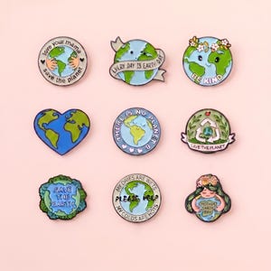 May include: A collection of nine circular and heart-shaped enamel pins featuring Earth-themed illustrations. Designs include globes with text such as 'love your mama', 'EVERY DAY IS EARTH DAY', 'BE KIND', 'THERE IS NO PLANET B', 'SAVE THE PLANET', 'SAVE THE EARTH', 'PLEASE HELP', and 'MOTHER EARTH DAY'.